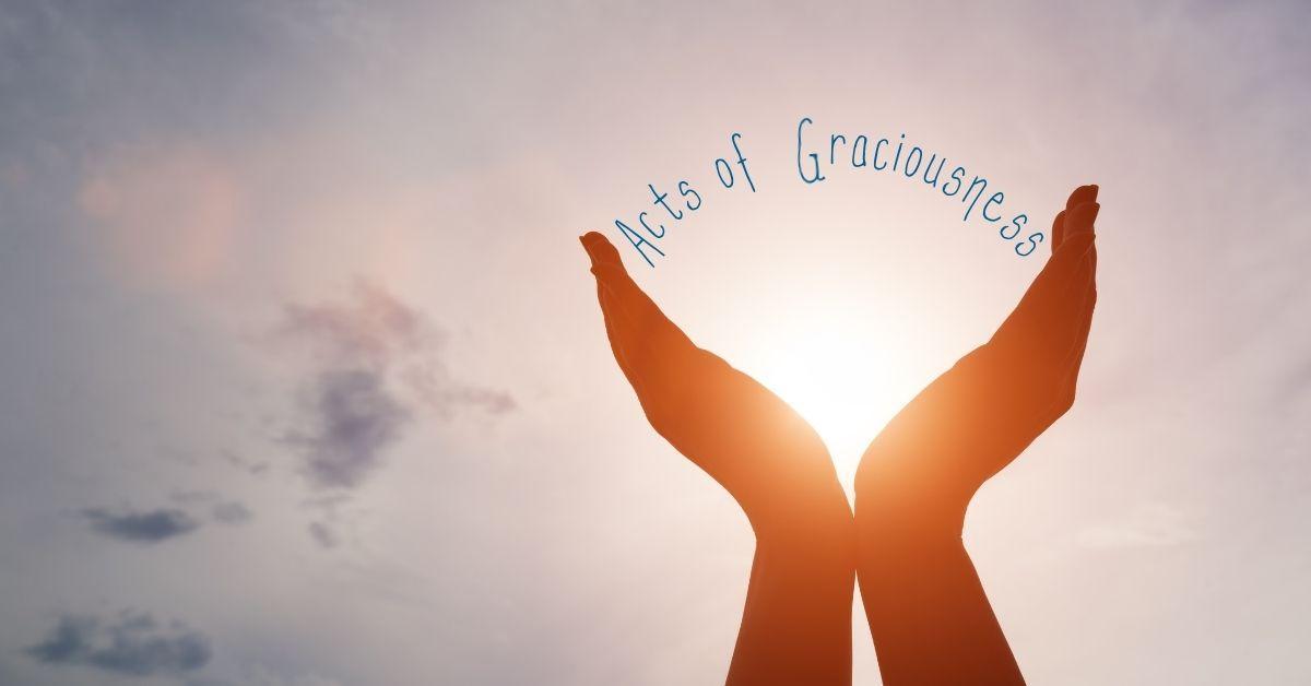 hands holding up the word acts of graciousness with the sun shining through
