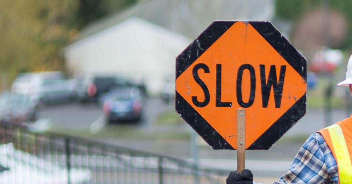 Image of a slow sign in orange and black being held by a flagger on a highway construction site.